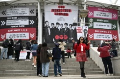 Des fans posent pour des photos devant une grande banderole à l'effigie du boys band de K-pop BTS, sur les marches menant au stade où le groupe se produira, à Goyang, le 9 avril 2026 - © AFP - Jung Yeon-je