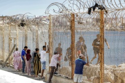 Des proches de migrants ayant traversé la frontière entre le Maroc et l'enclave espagnole de Ceuta voient passer des personnes refoulées derrière un grillage, dans la ville marocaine de Fnideq, le 2 août 2026 - © AFP - Abdel Majid BZIOUAT