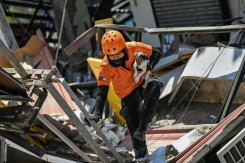 Un secouriste porte un chien lors d'une opération de recherche et de sauvetage dans un bâtiment effondré après un puissant séisme à General Santos, le 9 juin 2026 aux Philippines - © AFP - Jam STA ROSA