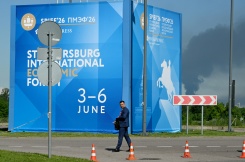 Un homme passe devant des affiches du Forum économique international de Saint-Pétersbourg alors que de la fumée s'élève en arrière-plan après des frappes de drones ukrainiens, le 3 juin 2026 en Russie - © AFP - STRINGER